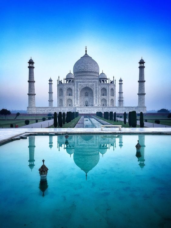 Taj Mahal ao amanhecer, com o céu azul refletido no espelho d'água